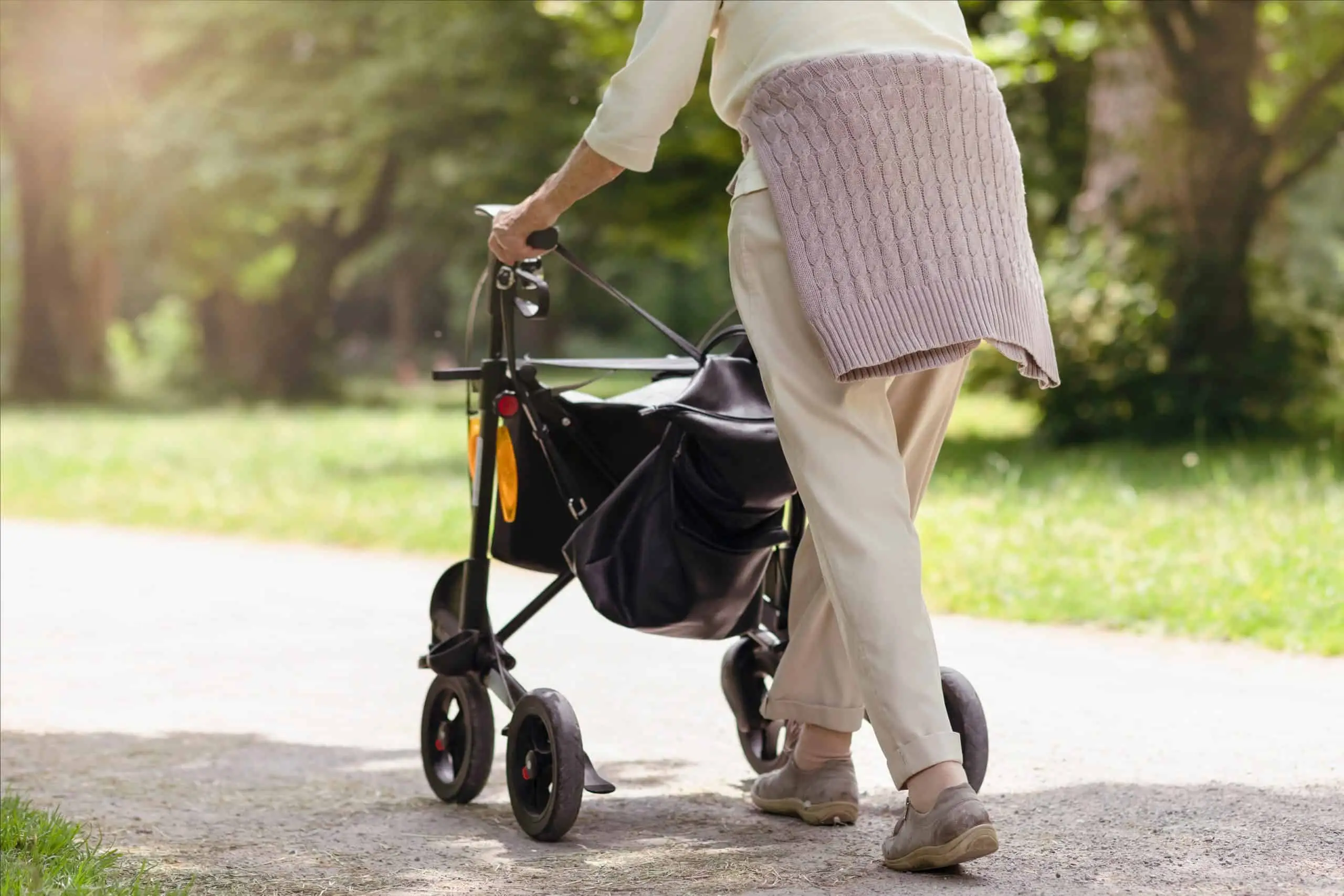Ältere Frau geht mit einem Rollator auf einem sonnigen Weg im Park – Symbol für Mobilität, Pflegegrade, Pflegestufen, Selbstständigkeit und Pflegeleistungen im Alter.