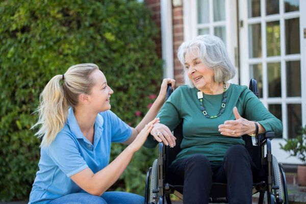 Junge Betreuungskraft im Gespräch mit einer Seniorin im Rollstuhl im Garten – individuelle Betreuung mit Herz.