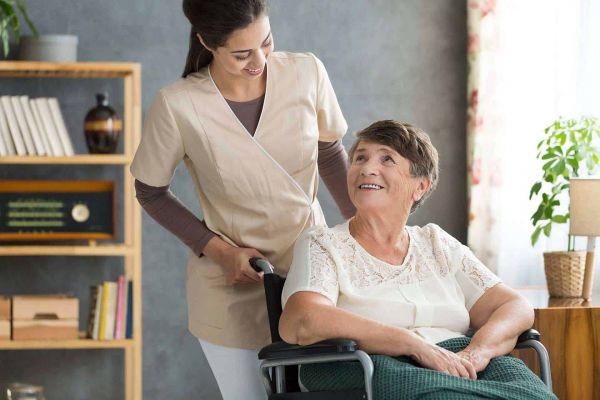 Pflegerin unterstützt eine Seniorin im Rollstuhl zu Hause – freundliche Betreuung in vertrauter Umgebung.