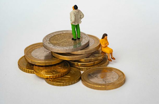 Stapel aus Euro‑Münzen mit zwei kleinen Miniaturfiguren – Symbolbild für steigende Pflegekosten, Mietdruck und finanzielle Belastung in Ballungsräumen.