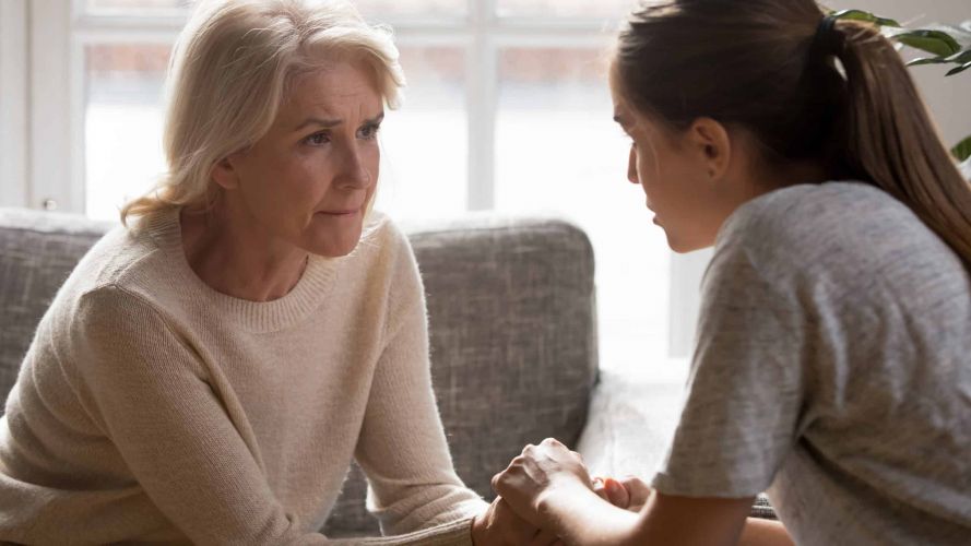 Erwachsene Tochter hält die Hände ihrer älteren Mutter, um sie in einem sensiblen Gespräch über Pflege und Unterstützung zu trösten und zu begleiten