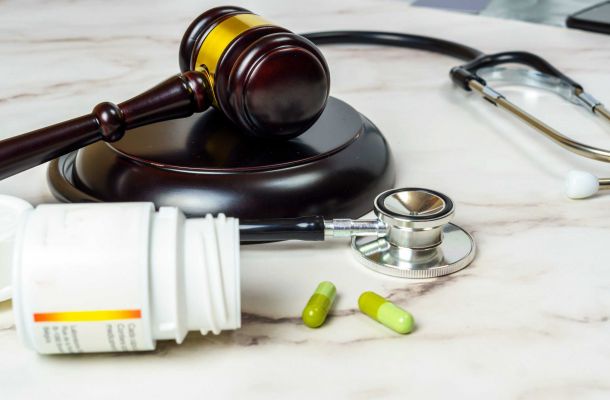 Symbolbild mit Richterhammer, Stethoskop, Tabletten und Medikamentendose auf Marmoruntergrund – Darstellung der Schnittstelle zwischen Gesundheitswesen und Gesetzgebung.