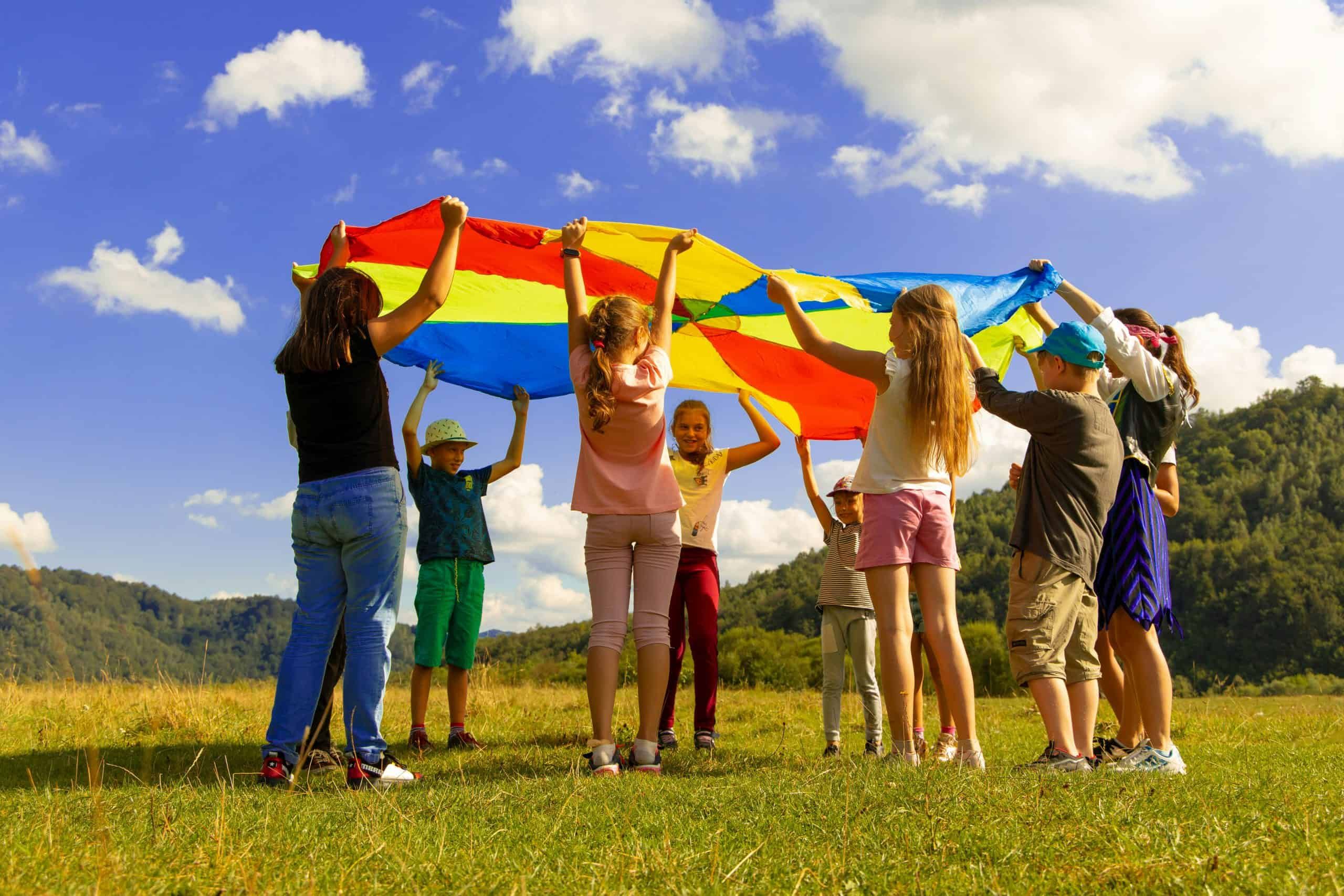 Gruppe von Kindern hebt gemeinsam ein buntes Tuch im Freien – Unterstützung durch Ihr Team 24 für das Schifferkinderheim Mannheim
