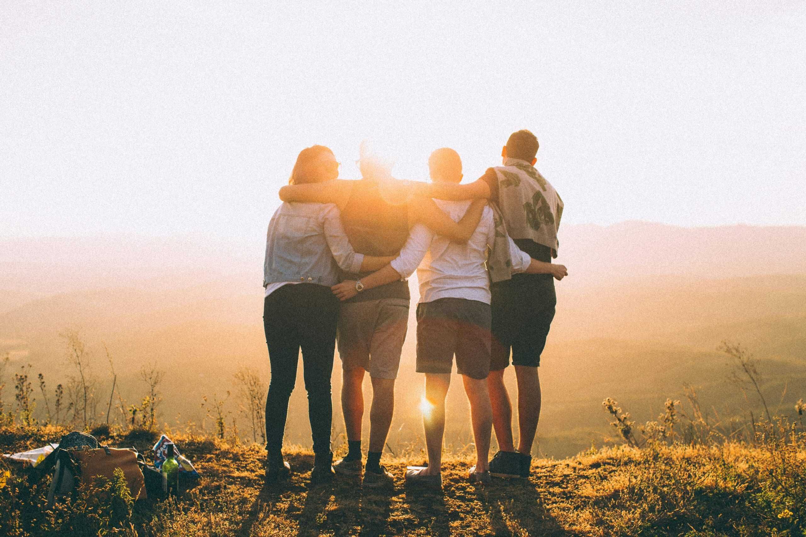Vier Menschen stehen Arm in Arm im Sonnenuntergang und blicken in die Ferne – Symbol für Zusammenhalt, Teamgeist und internationale Karrierechancen bei Ihr Team 24