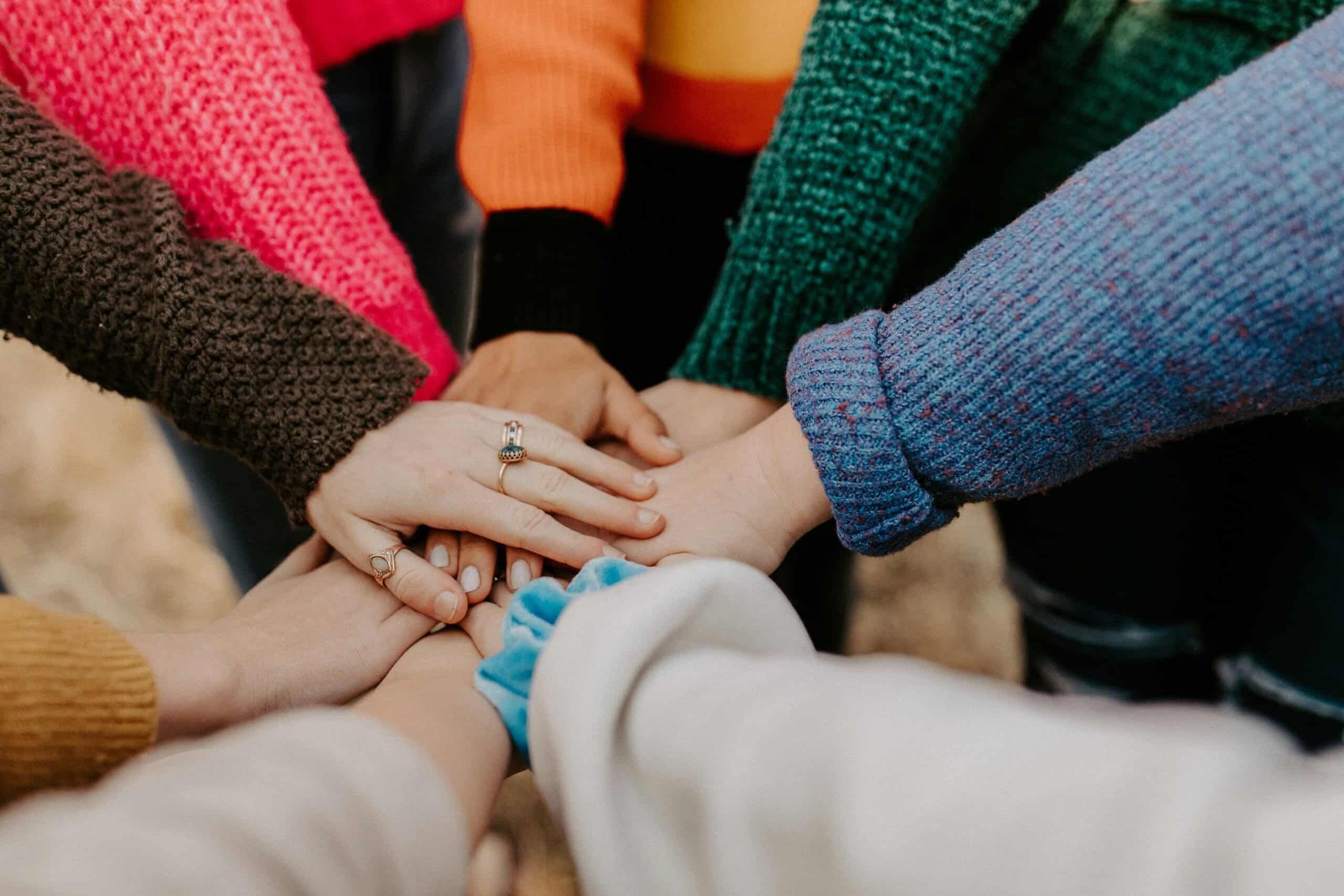 Mehrere Hände von Menschen liegen übereinander als Symbol für Vertrauen, Zusammenhalt und Teamarbeit bei Ihr Team 24