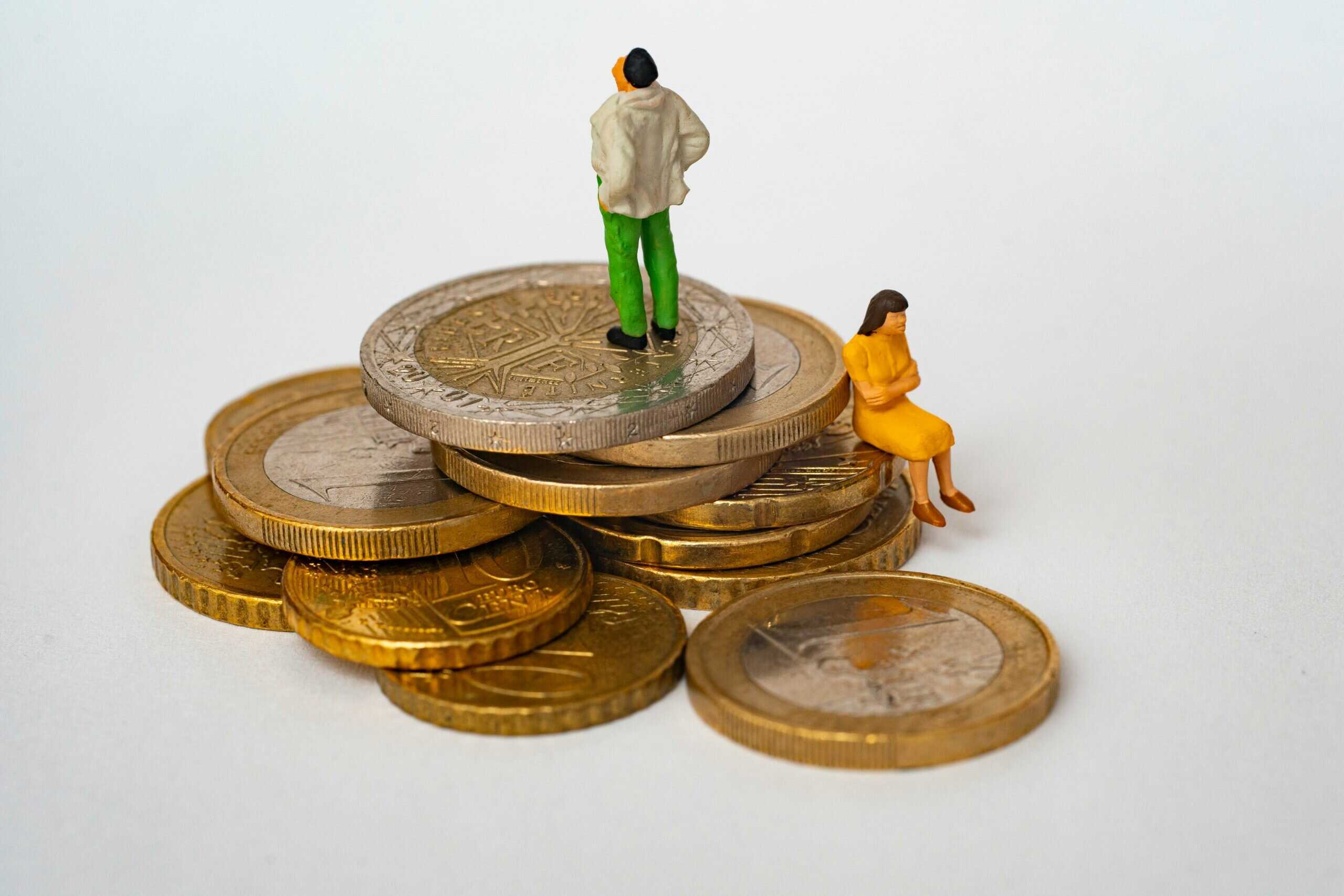 Stapel aus Euro‑Münzen mit zwei kleinen Miniaturfiguren – Symbolbild für steigende Pflegekosten, Mietdruck, häusliche Betreuung und finanzielle Belastung in Ballungsräumen.