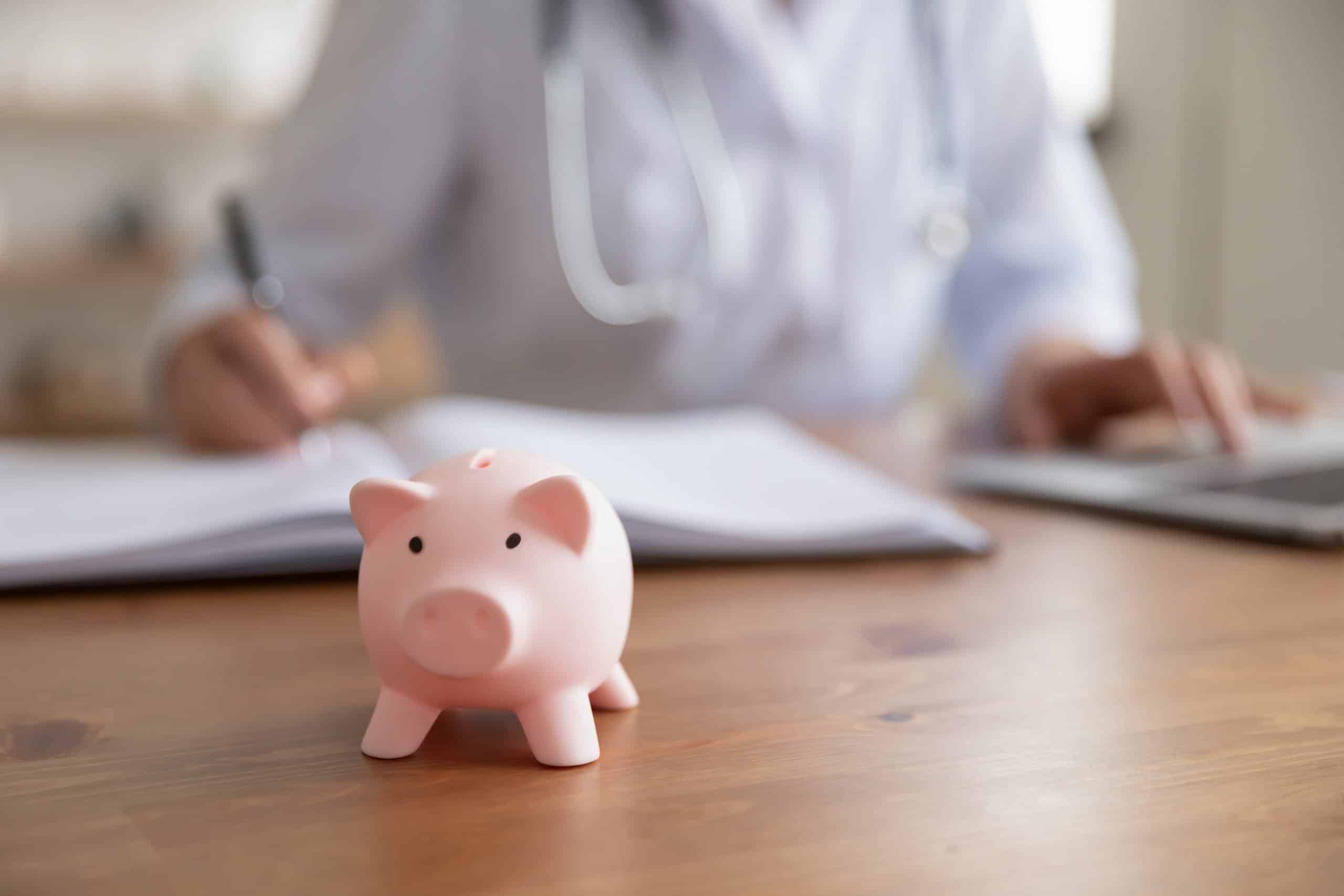 Sparschwein auf einem Tisch mit Pfleger im Hintergrund – Symbolbild für die Abrechnung mit der Pflegekasse.