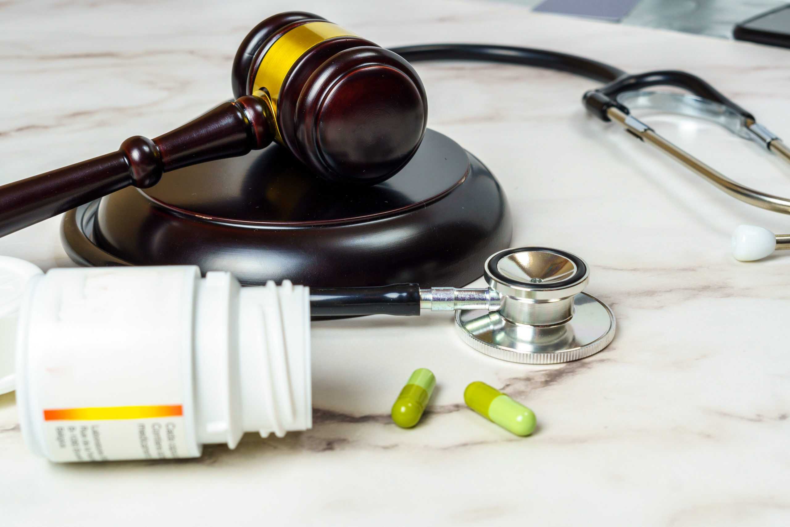 Symbolbild für neues Pflegegesetz mit Richterhammer, Stethoskop, Tabletten und Medikamentendose auf Marmoruntergrund – Darstellung der Schnittstelle zwischen Gesundheitswesen und Gesetzgebung.