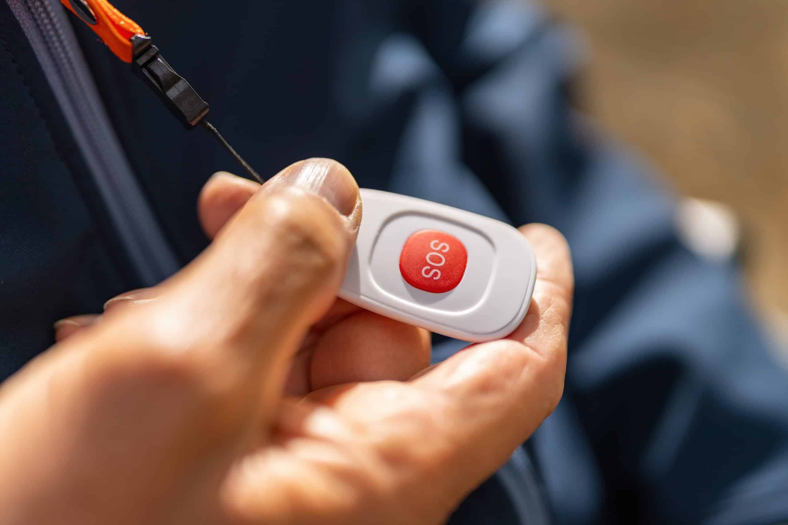 Nahaufnahme einer Hand mit einem mobilen SOS-Hausnotrufsender zur Auslösung eines Notfalls.