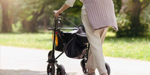 Ältere Frau geht mit einem Rollator auf einem sonnigen Weg im Park – Symbol für Mobilität, Pflegegrade, Pflegestufen, Selbstständigkeit und Pflegeleistungen im Alter.