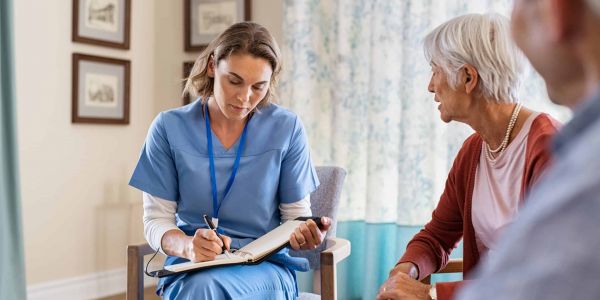 Pflegefachkraft im Gespräch mit älterer Frau bei einem Pflegeberatungseinsatz § 37 Abs. 3 zu Hause, dokumentiert Informationen in einem Notizbuch