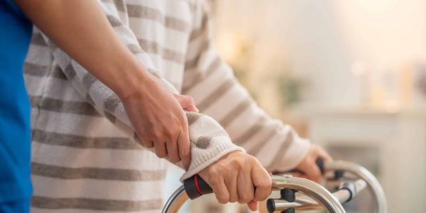 Eine Hand einer Pflegekraft unterstützt eine Frau am Rollator um hier 24 Stunden Betreuung rechtlich sicher zu symbolisieren.