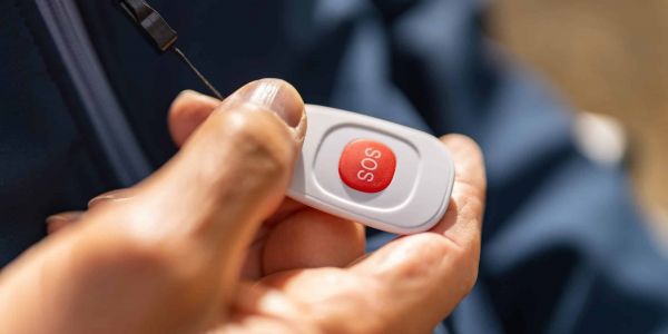 Nahaufnahme einer Hand mit einem mobilen SOS-Hausnotrufsender zur Auslösung eines Notfalls.