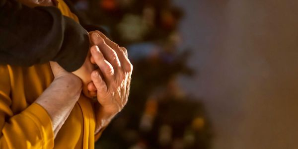 Nahaufnahme von zwei Händen, die sich an Weihnachten liebevoll halten; symbolisiert Nähe, Unterstützung und häusliche Betreuung.
