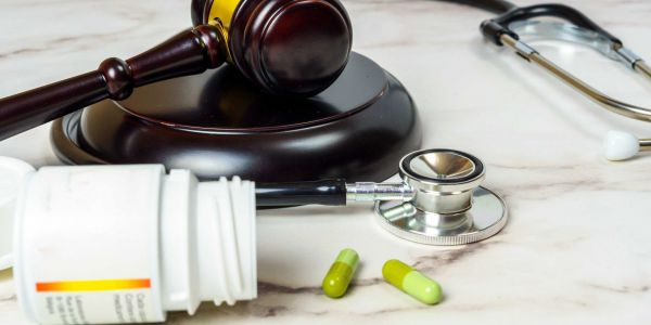 Symbolbild mit Richterhammer, Stethoskop, Tabletten und Medikamentendose auf Marmoruntergrund – Darstellung der Schnittstelle zwischen Gesundheitswesen und Gesetzgebung.