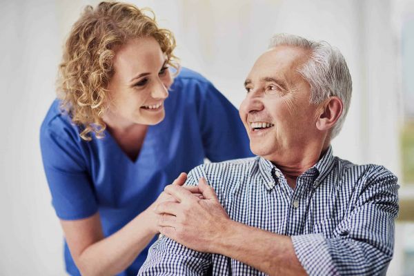 Pflegekraft spricht lächelnd mit Senior – wertschätzende Betreuung im eigenen Zuhause.