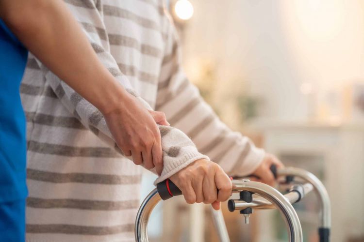 Eine Hand einer Pflegekraft unterstützt eine Frau am Rollator um hier 24 Stunden Betreuung rechtlich sicher zu symbolisieren.